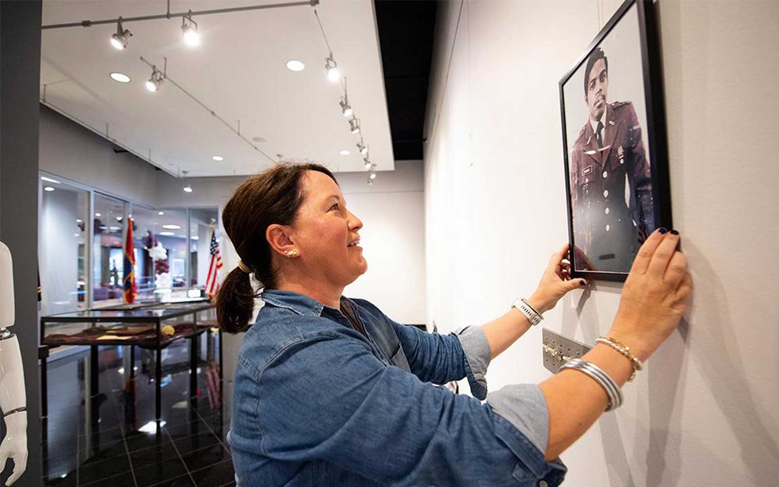 University Archivist Jessica Perkins-Smith adjusts a framed picture of Col. Robert L. Barnes Jr., one of Mississippi State’s earliest Black graduates and ROTC members, featured in the current art exhibit “Student Salutes: A Visual Tribute to MSU Veterans” in the Colvard Student Union Art Gallery. Barnes was awarded an MSU Doctor of Public Service Degree in 2022. (Photo by Grace Cockrell) 